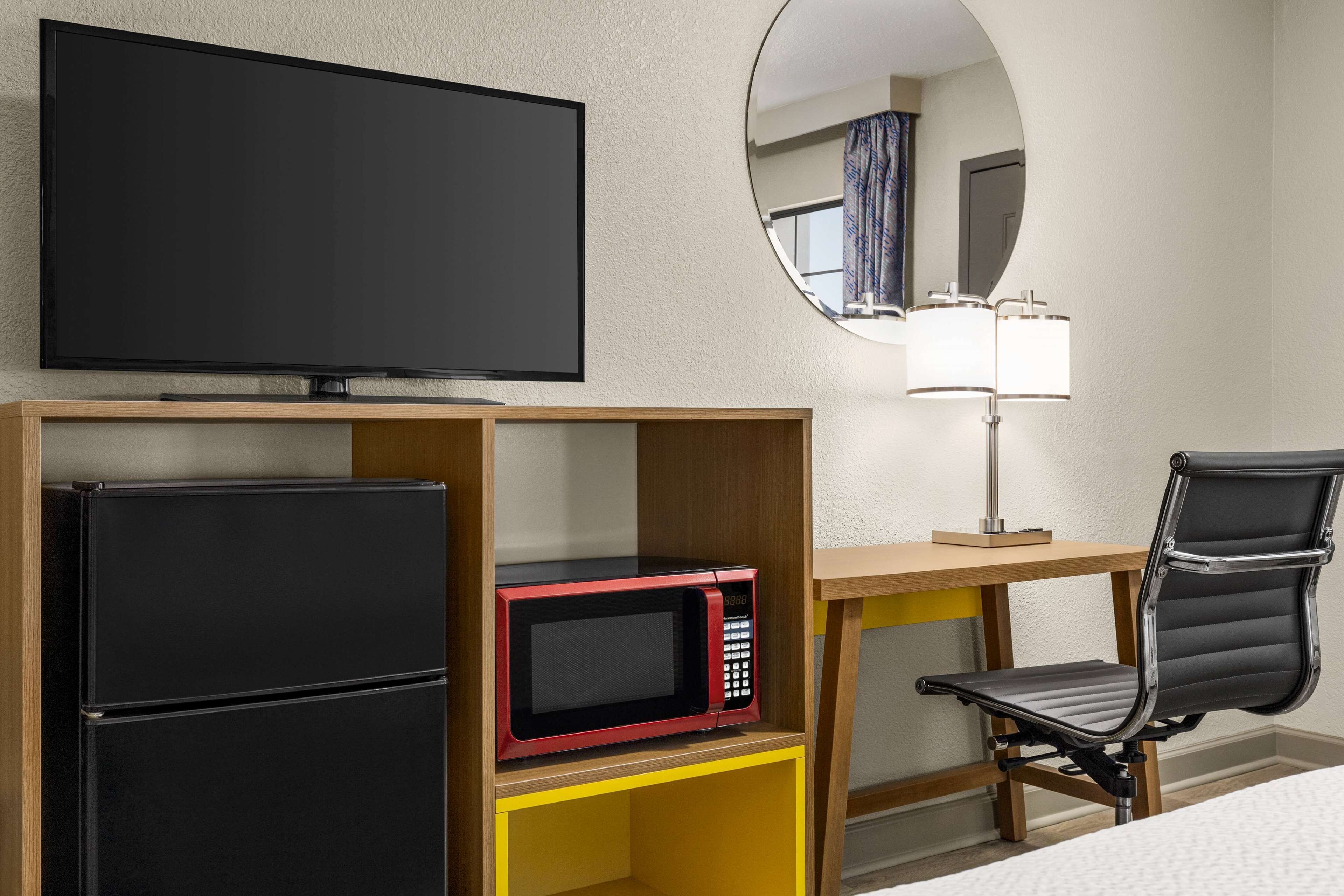 Une chambre d’hôtel équipée d’une télévision à écran plat, d’un four à micro-ondes, d’un réfrigérateur, d’un bureau avec une lampe et d’une chaise.