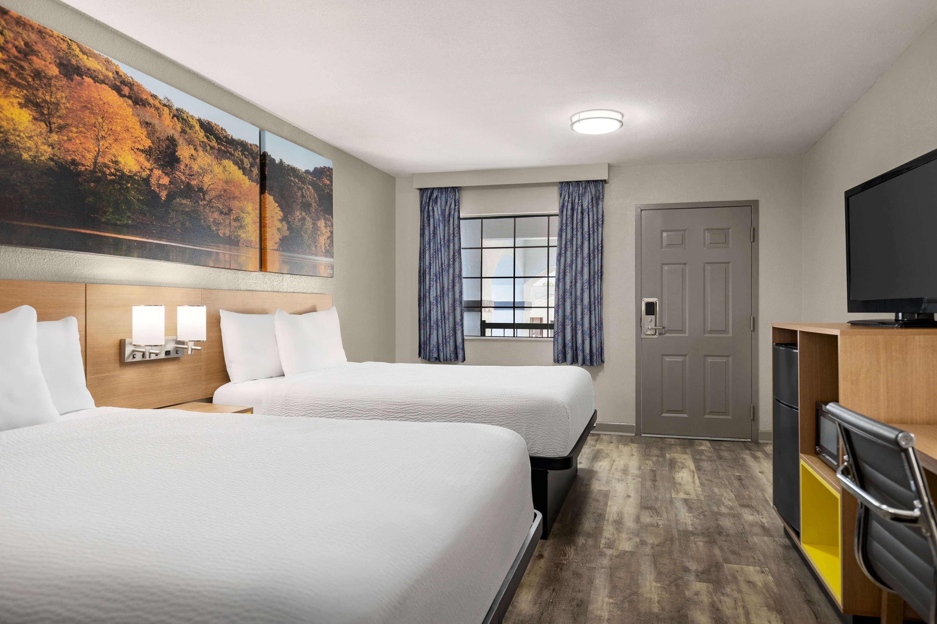 Habitación de hotel con dos camas, un ventanal con cortinas, un televisor y un armario de madera.