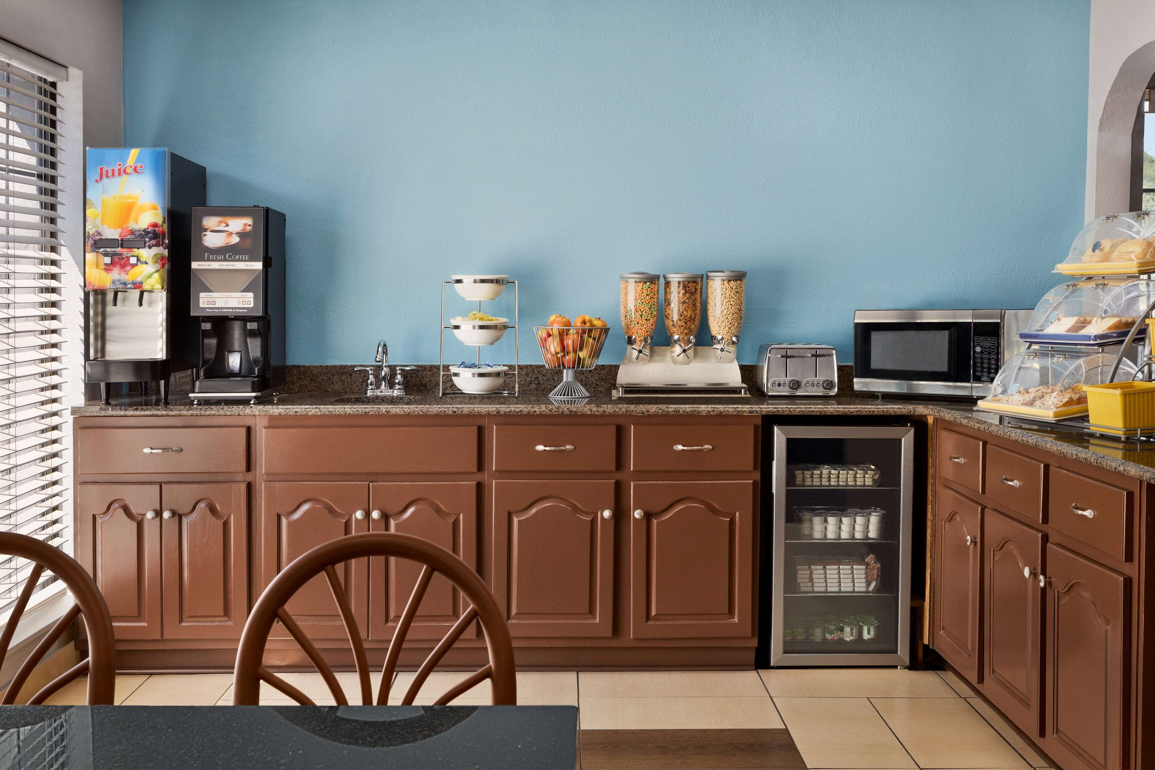 A kitchen with a juice dispenser, coffee maker, toaster, microwave, and a refrigerator with storage bins.
