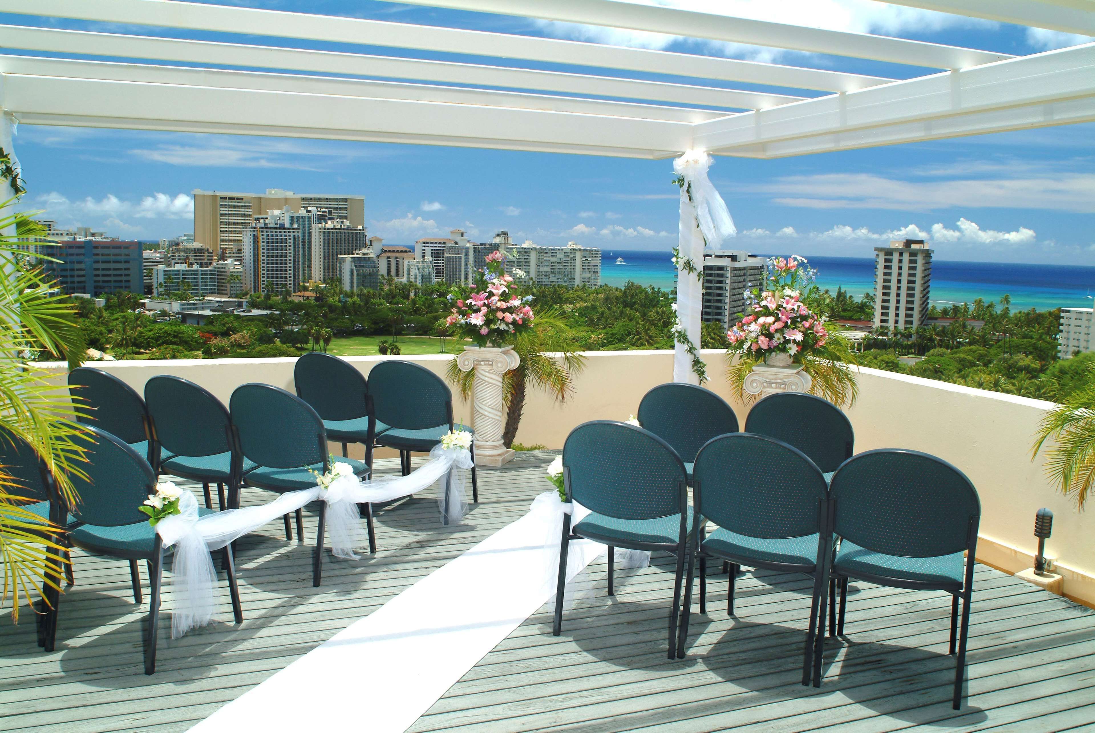 Una terraza con sillas y mesas dispuestas para un evento, con vistas a la ciudad y al océano.