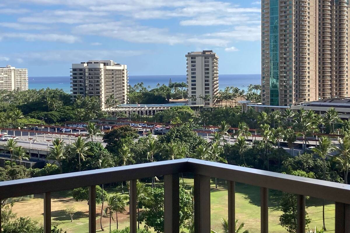 A high-rise hotel with multiple floors, a parking lot, and a view of the ocean.