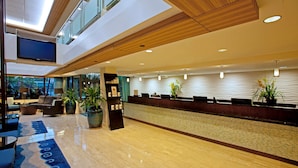A modern hotel lobby with a reception desk, seating area, and large windows.