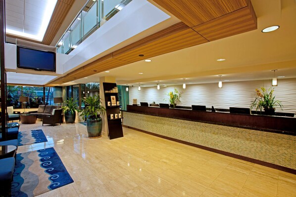 A modern hotel lobby with a reception desk, seating area, and large windows. - DoubleTree by Hilton Hotel Alana - Waikiki Beach (Honolulu)