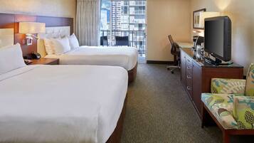 A hotel room with two beds, a television, a desk, and a view of the city through the window.