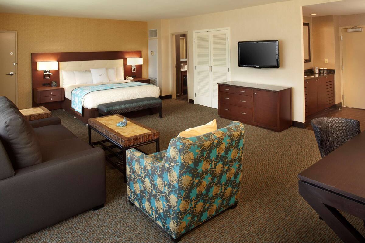 A hotel room with a bed, a sofa, a chair, a desk, and a television.