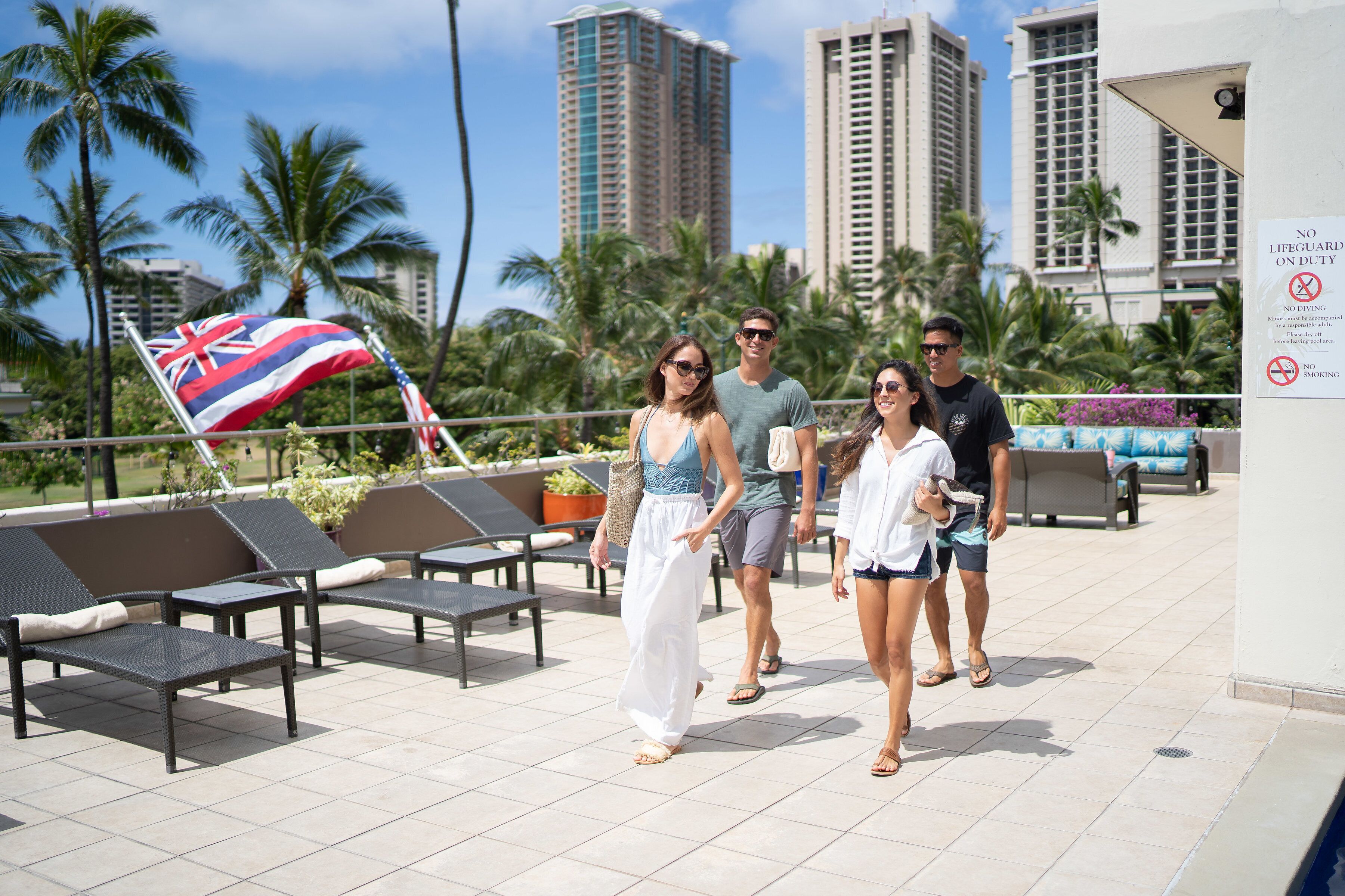A rooftop lounge area with lounge chairs, a flag, and a sign indicating no lifeguard on duty.