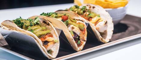 Three tacos with various toppings on a plate, accompanied by a bowl of chips.