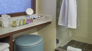 A bathroom with a vanity, a robe hanging on a rack, a round stool, and a glass shower enclosure.