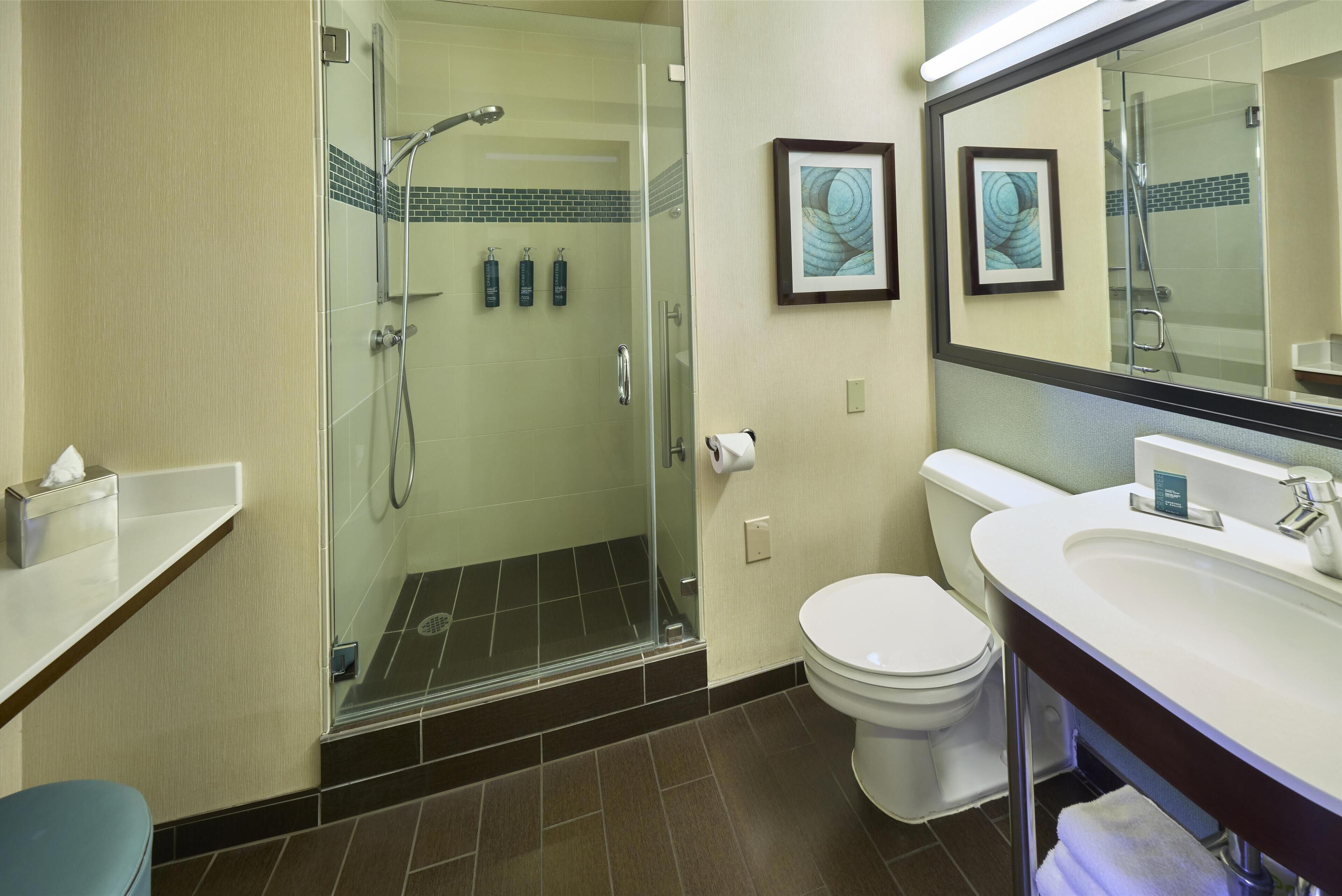 A modern bathroom with a glass-enclosed shower, a white toilet, and a sink with a mirror above it.
