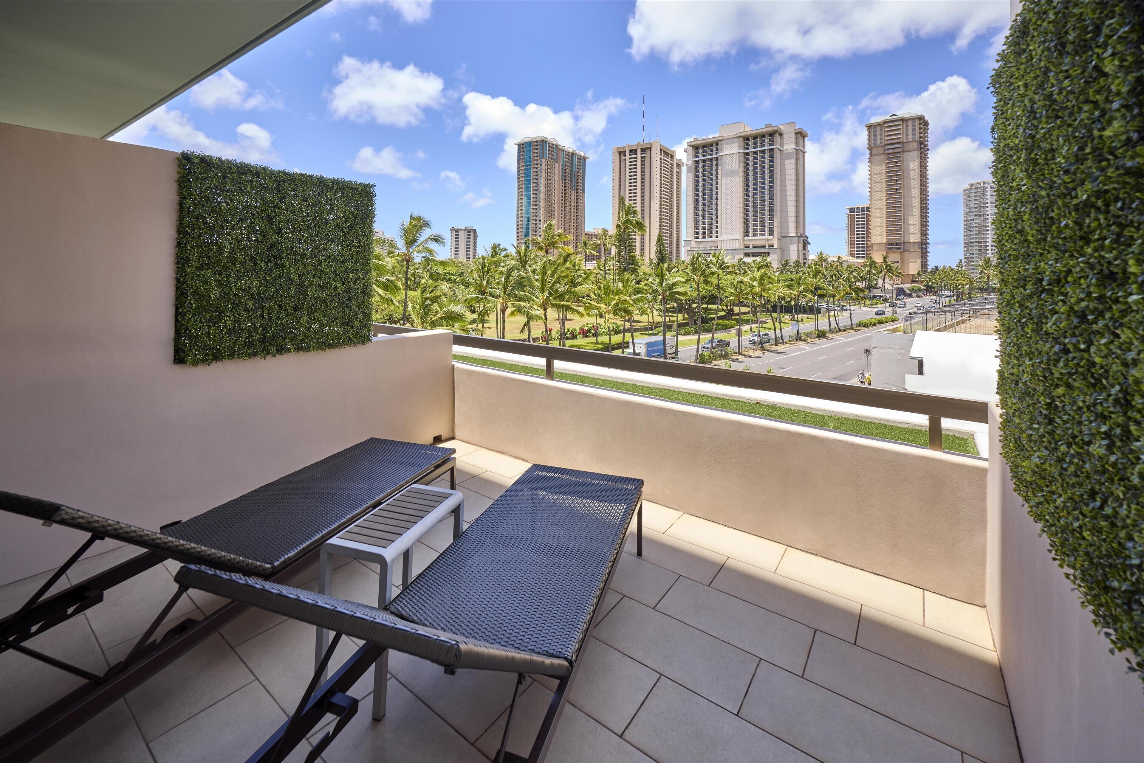A balcony with a view of tall buildings, a table, and a bench.
