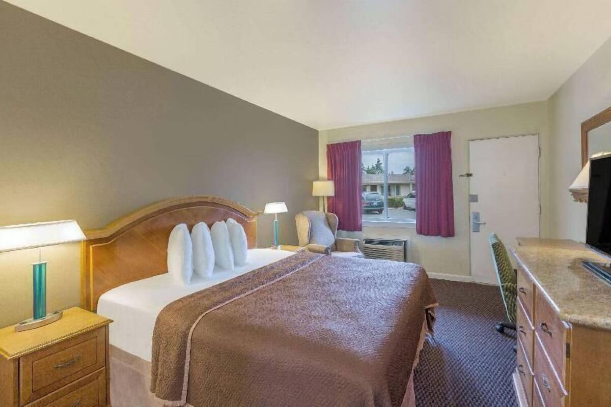 A hotel room with a bed, bedside lamps, a desk, a chair, a dresser, and a television.