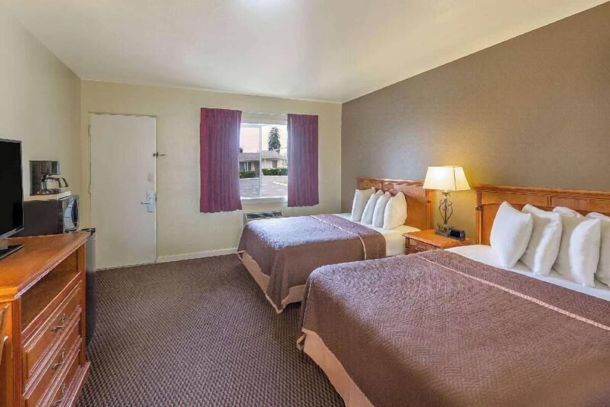 A hotel room with two beds, a television, a desk with a lamp, and a view of the outside.