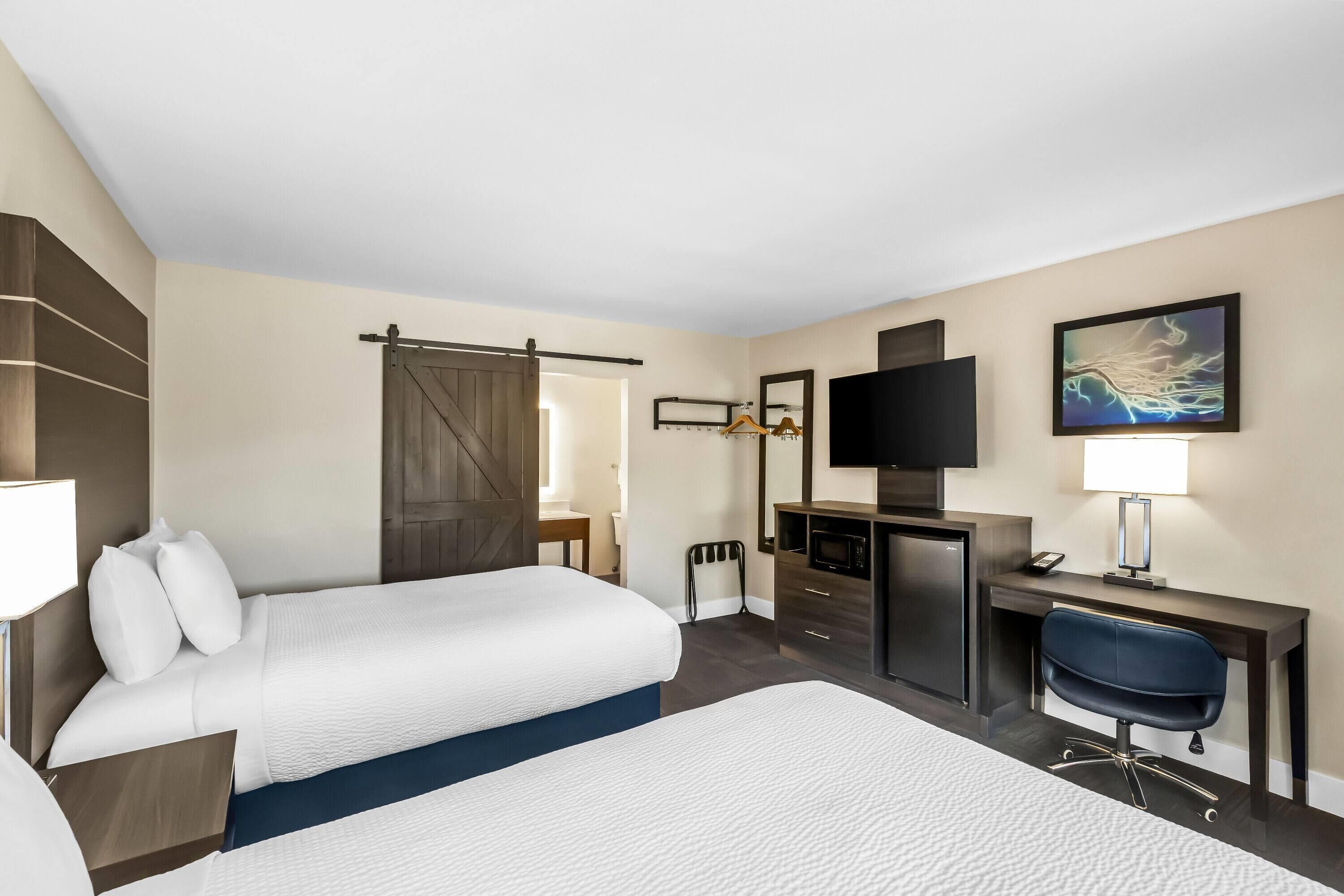 A hotel room with two beds, a desk, a chair, a TV, and a painting on the wall.