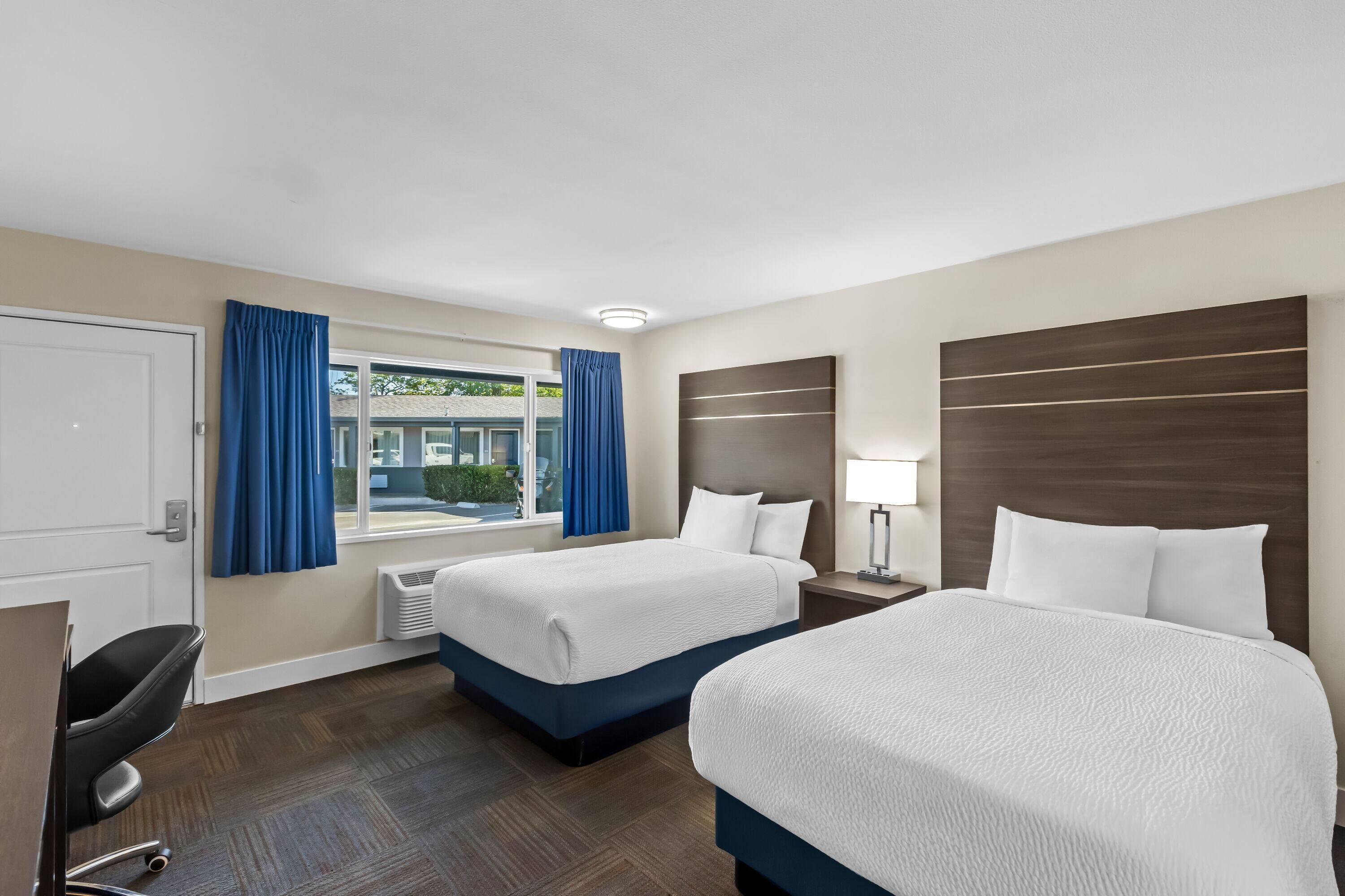 Een hotelkamer met twee bedden, een bureau, een stoel en een raam met gordijnen.