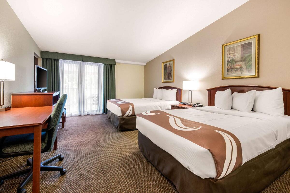 A hotel room with two beds, a desk, a chair, a TV, and a painting on the wall.