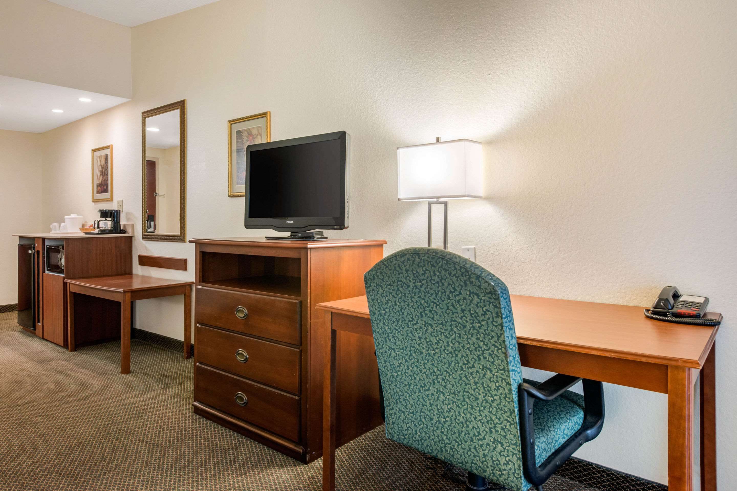 Una habitación de hotel con un escritorio de madera, un televisor, una lámpara, una silla y un aparador.
