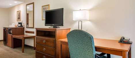 Una habitación de hotel con un escritorio de madera, un televisor, una lámpara, una silla y un aparador.