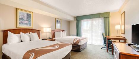 A hotel room with two beds, a desk, a chair, a TV, and a window with curtains.