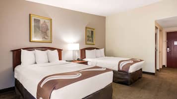 Habitación de hotel con dos camas, una mesita de noche con una lámpara y dos cuadros en la pared.
