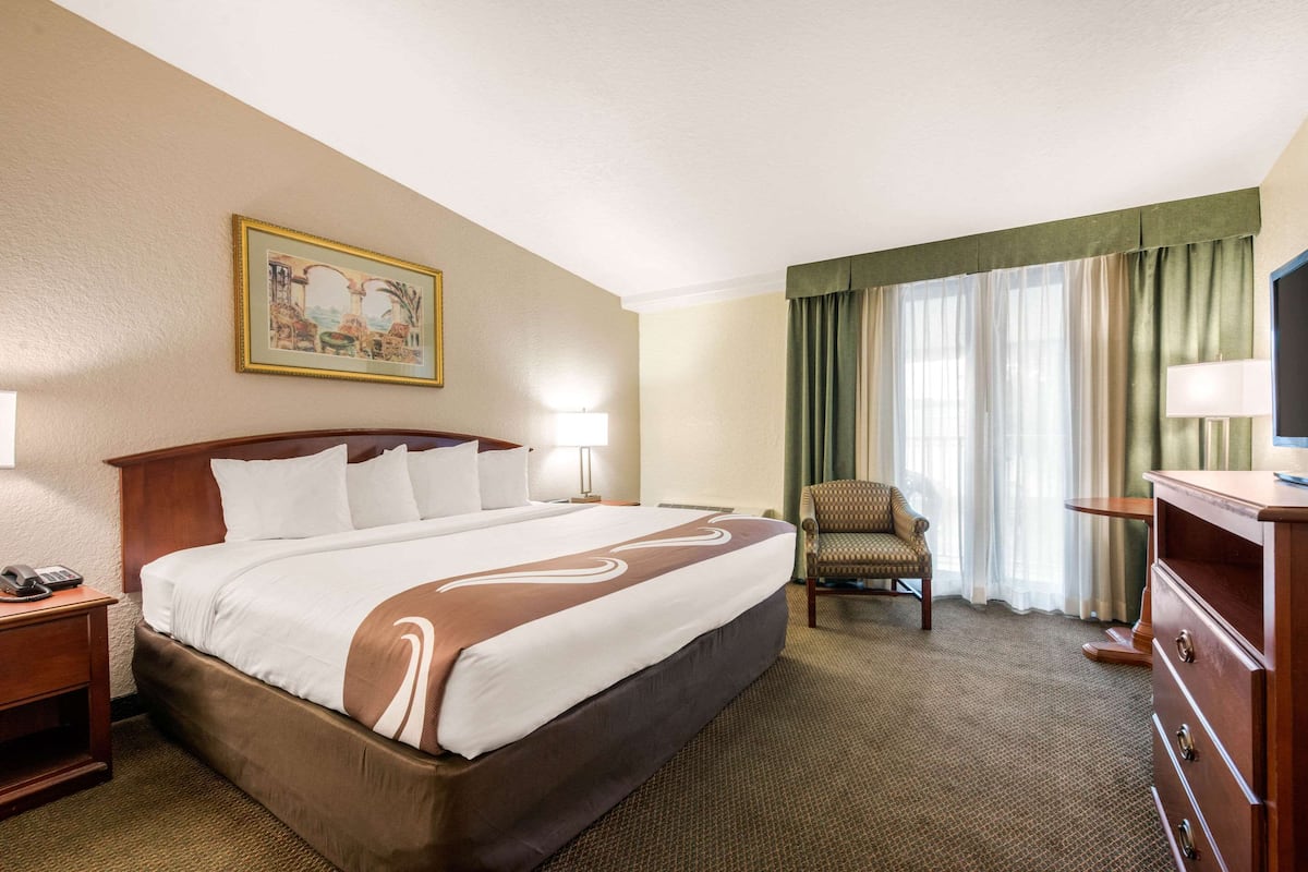 Habitación de hotel con una cama grande, una silla, un escritorio, una lámpara y un cuadro en la pared.
