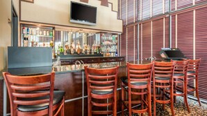 A bar area with wooden chairs, a counter with bottles, and a TV mounted on the wall. - Quality Inn & Suites Tarpon Springs South (Tarpon Springs)