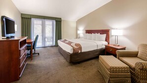 A hotel room with a bed, a desk with a television, a chair, a nightstand with a lamp, and a view of the outdoors through the window. - Quality Inn & Suites Tarpon Springs South (Tarpon Springs)