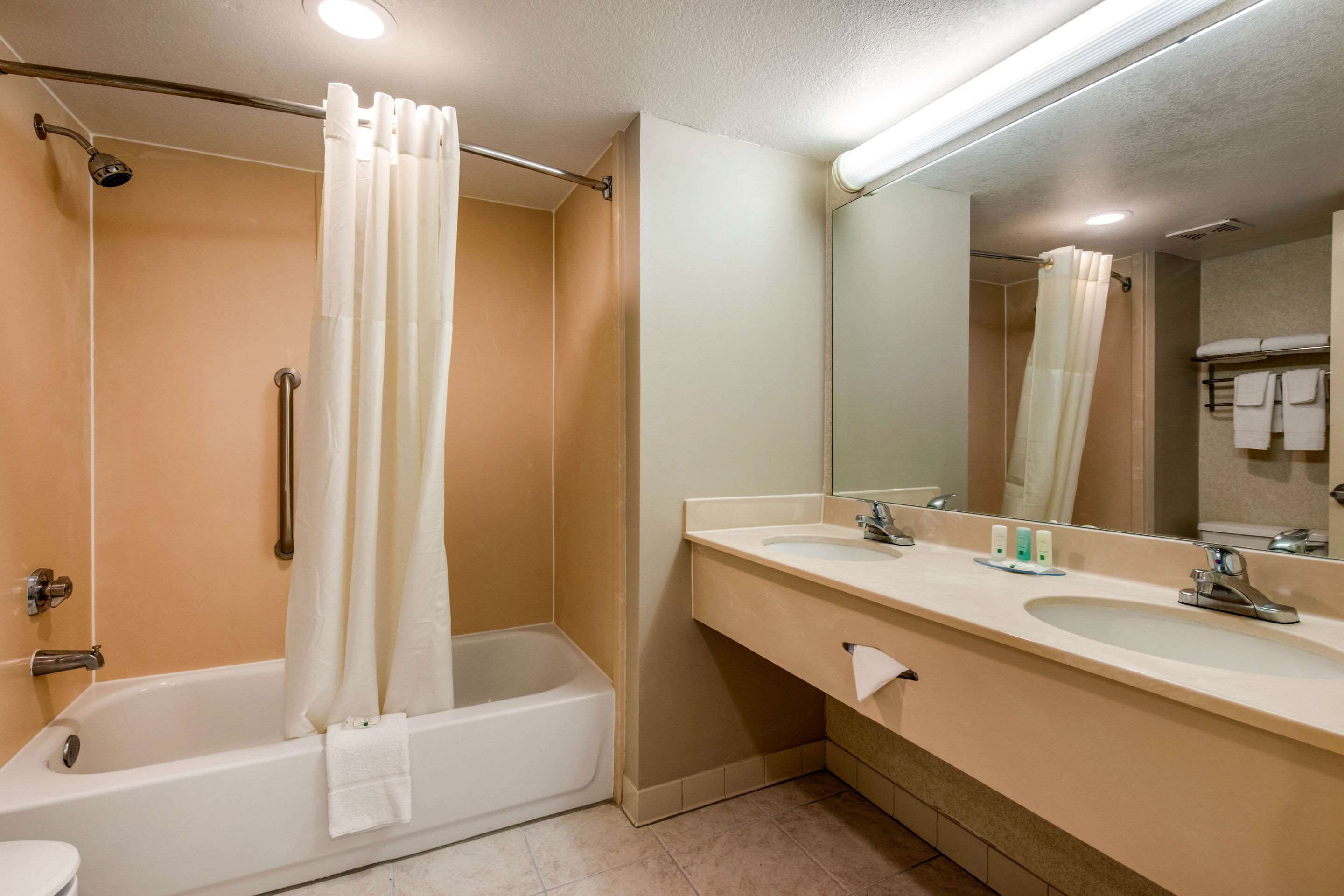 A bathroom with a bathtub, two sinks, a mirror, and a shower curtain.
