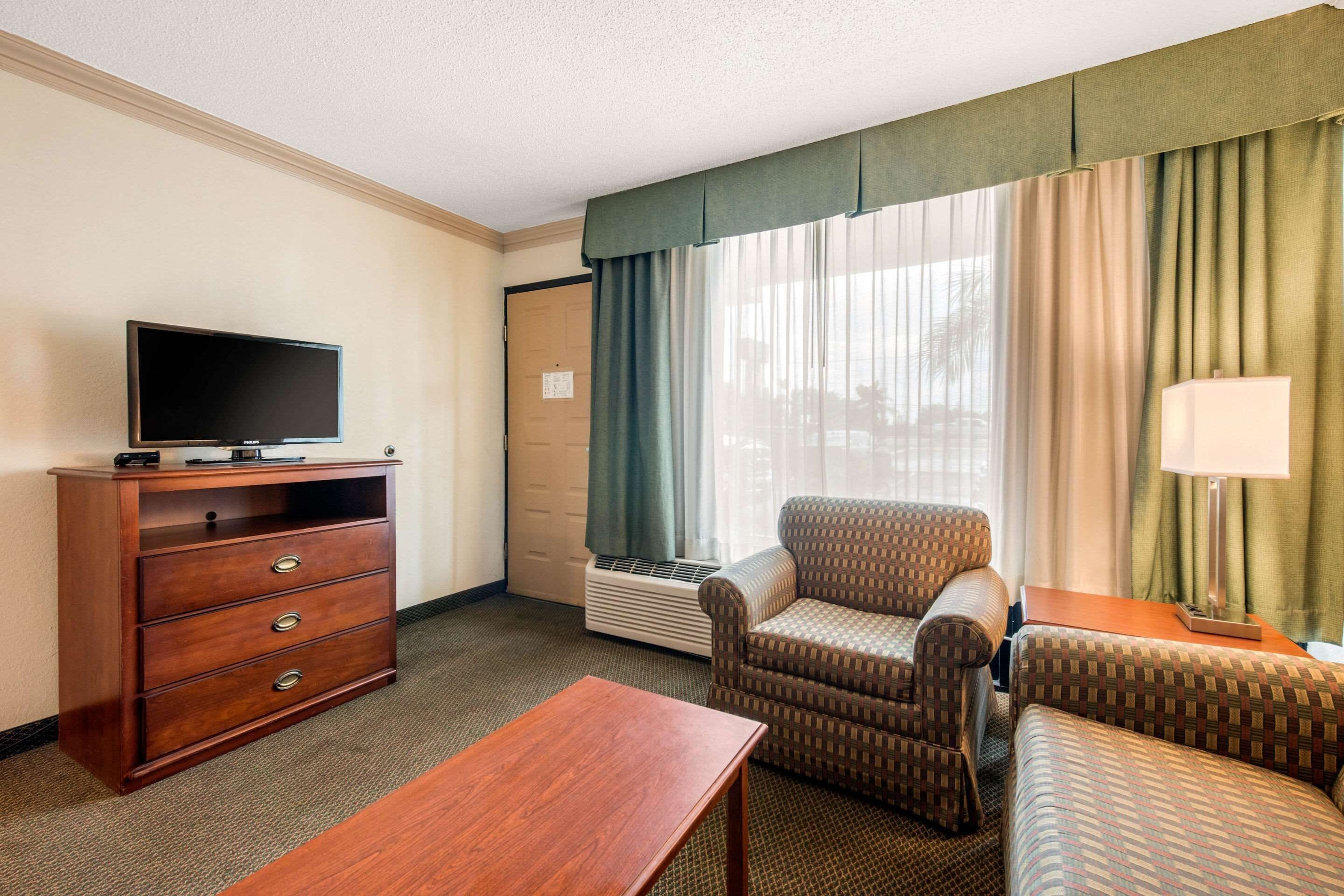 A hotel room with a flat-screen TV, a wooden dresser, a sofa, a chair, and a lamp.