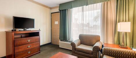 Habitación de hotel con televisión de pantalla plana, cómoda de madera, sofá, sillón y lámpara.