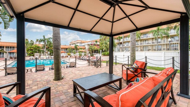 A covered outdoor seating area with a pool, lounge chairs, and a table. - Quality Inn & Suites Tarpon Springs South (Tarpon Springs)
