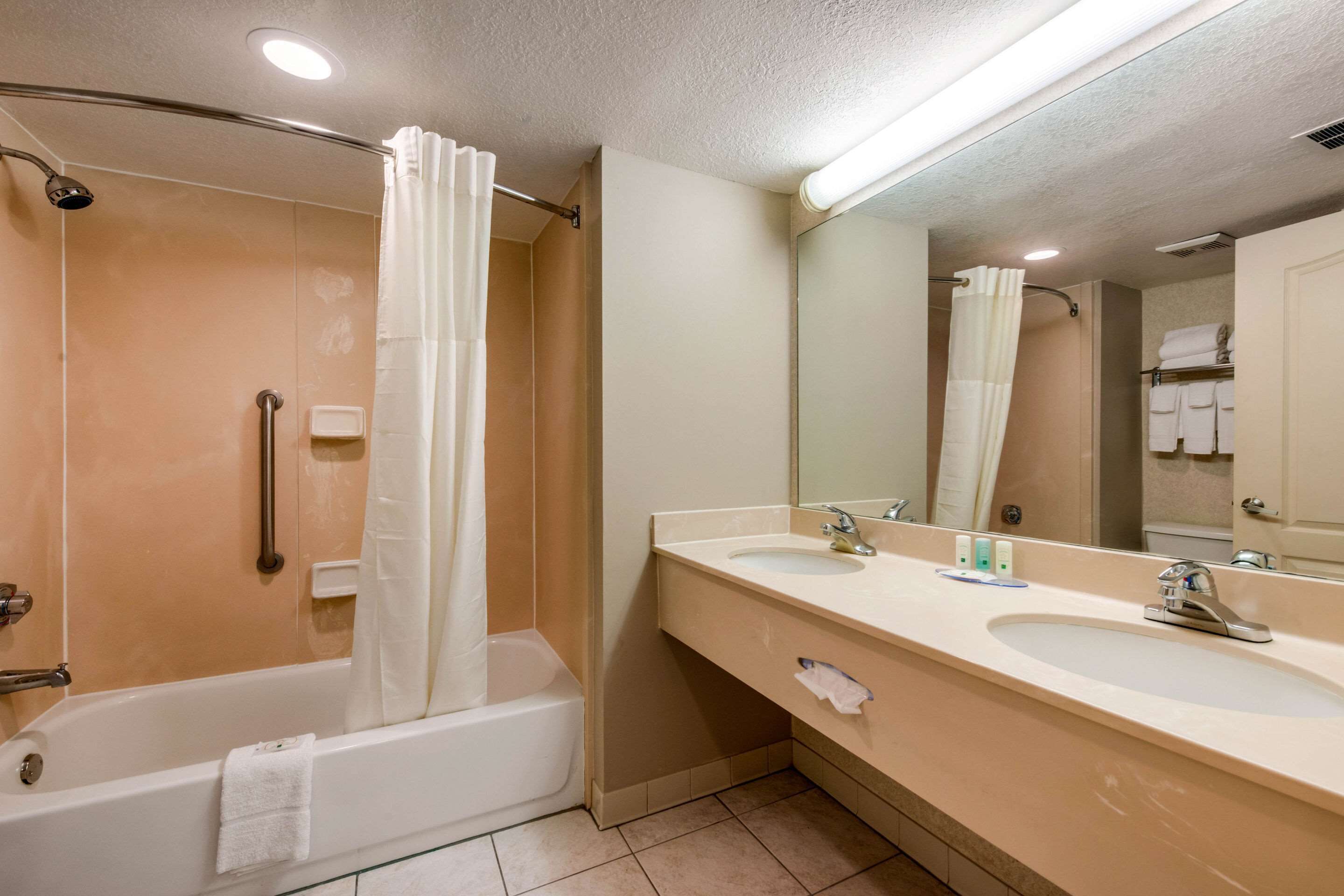 A bathroom with a bathtub, two sinks, a mirror, and a shower curtain.