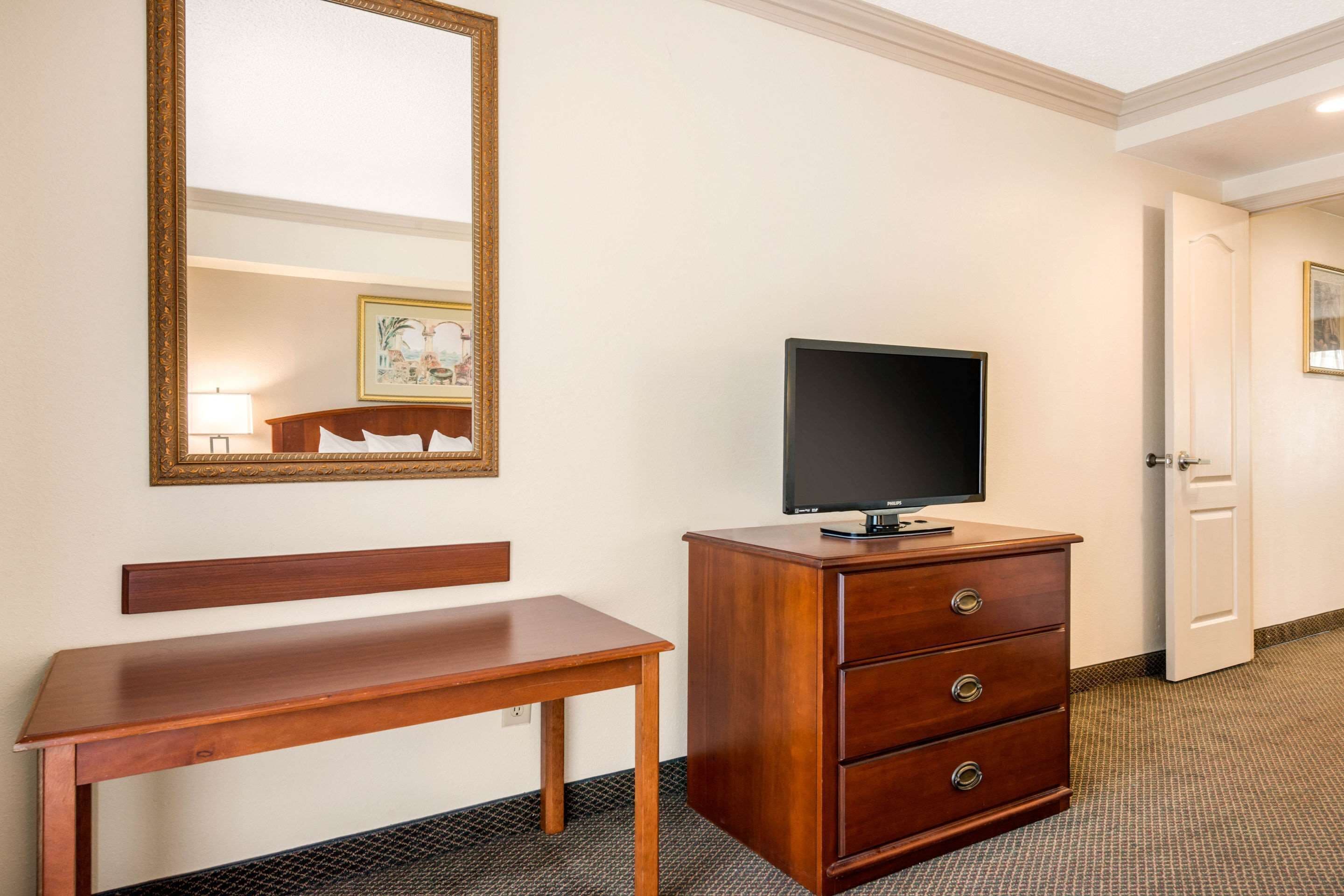 A hotel room with a wooden bench, a TV on a wooden dresser, and a door leading to another room.