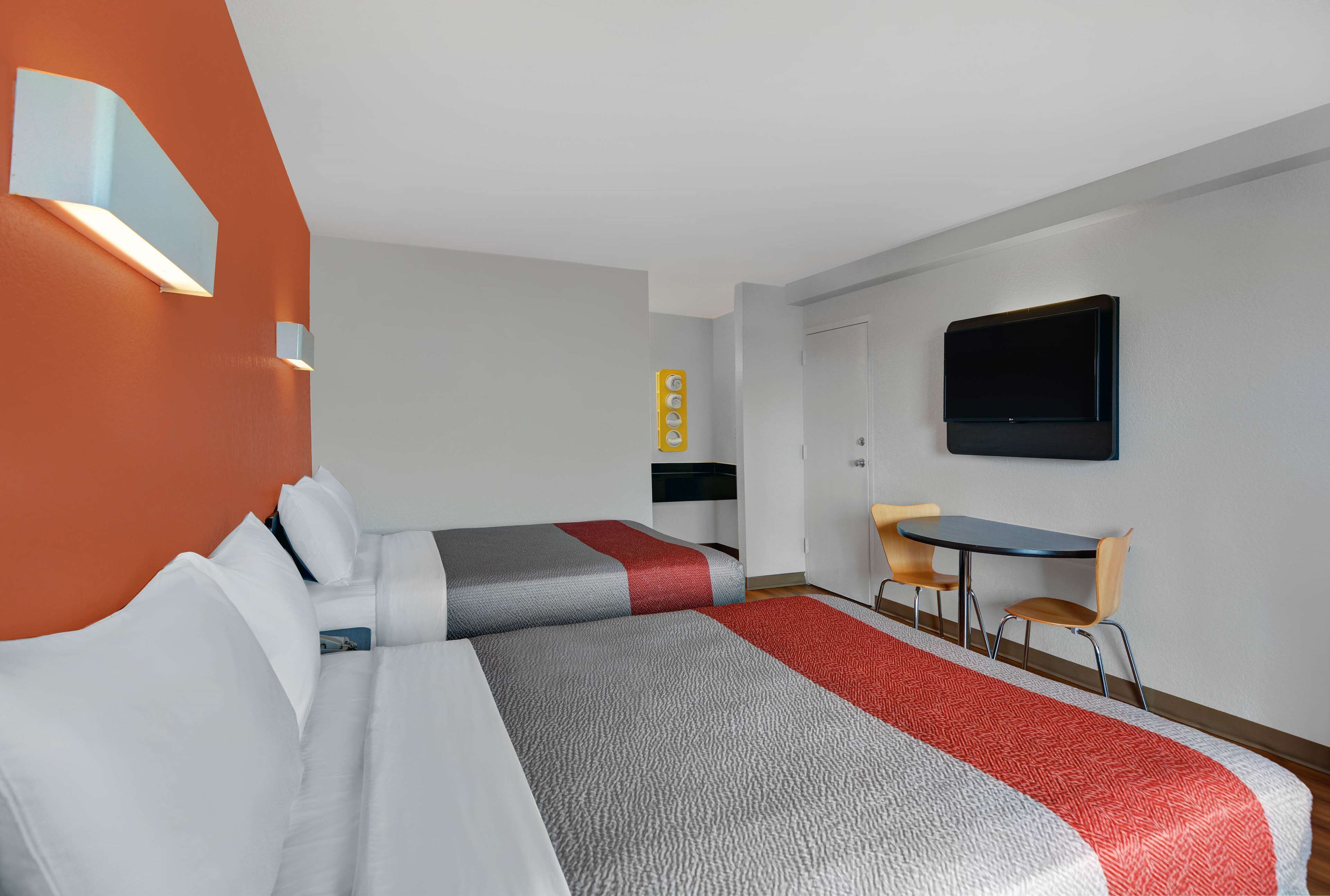 Hotellihuone, jossa on kaksi sänkyä, työpöytä, tuoli, televisio ja seinään kiinnitetty valaisin.