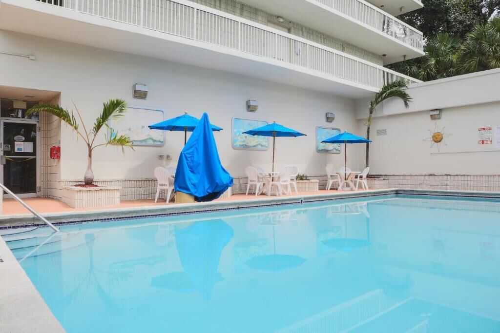 An indoor swimming pool with blue umbrellas, white chairs, and a white wall with artwork.