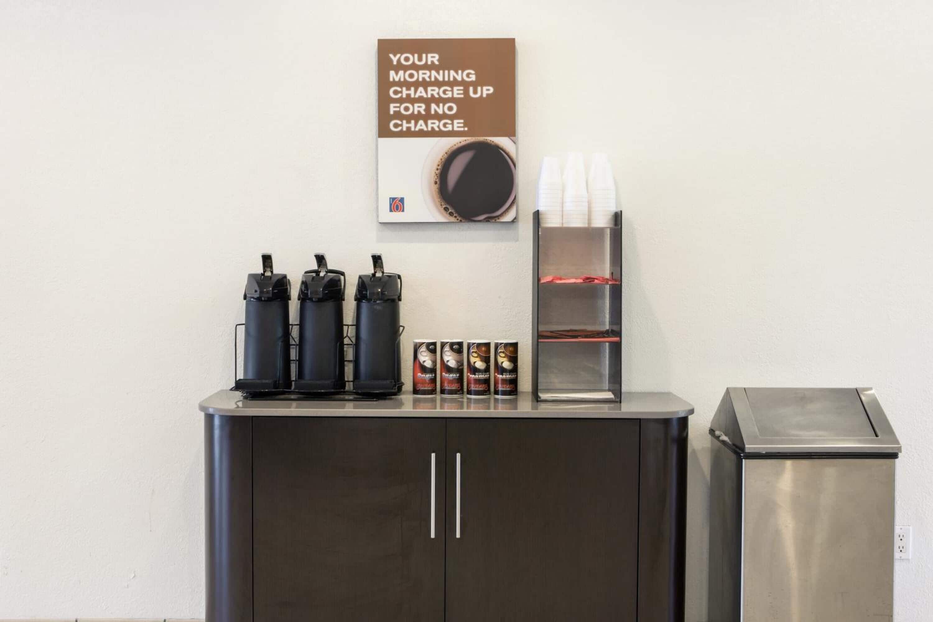 A coffee station with multiple coffee machines, disposable cups, and a trash bin.