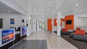 Un hall d’accueil d’hôtel comprenant un comptoir de réception, un espace salon et un couloir menant aux autres chambres.