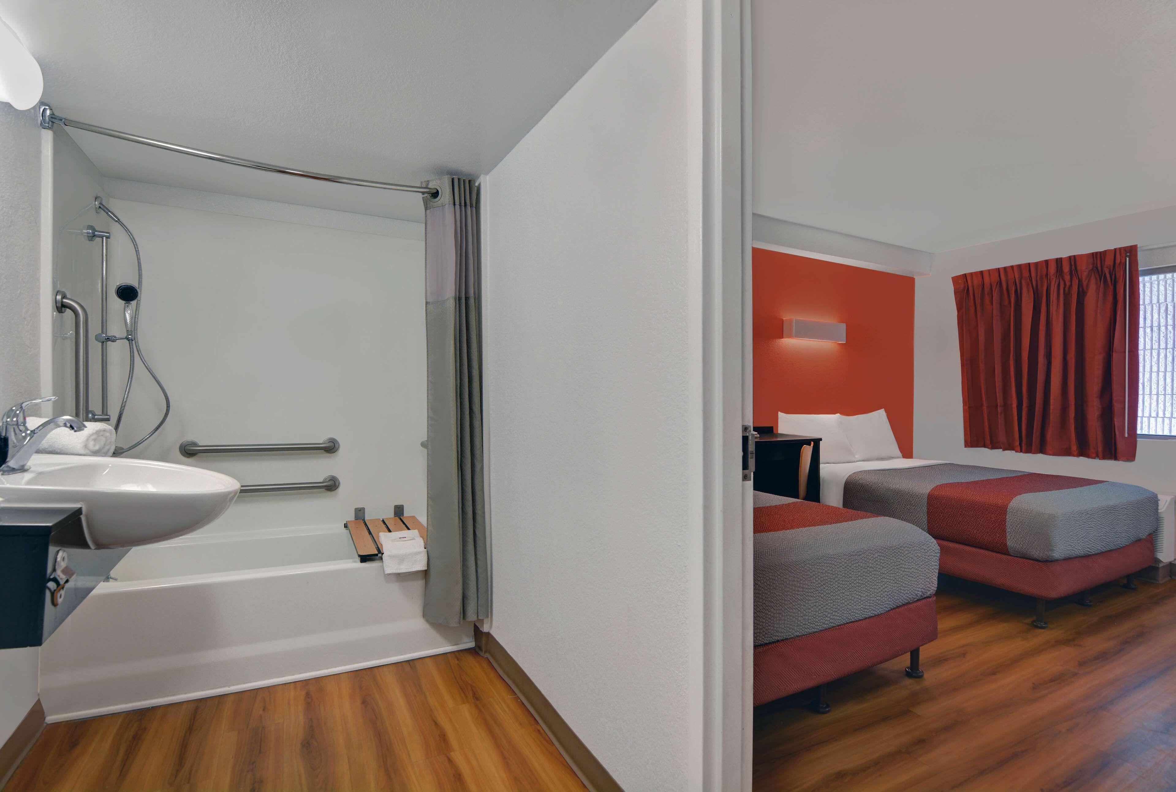Une salle de bain moderne équipée d’un lavabo, d’une douche et de toilettes. À côté se trouve une chambre avec deux lits et une fenêtre.