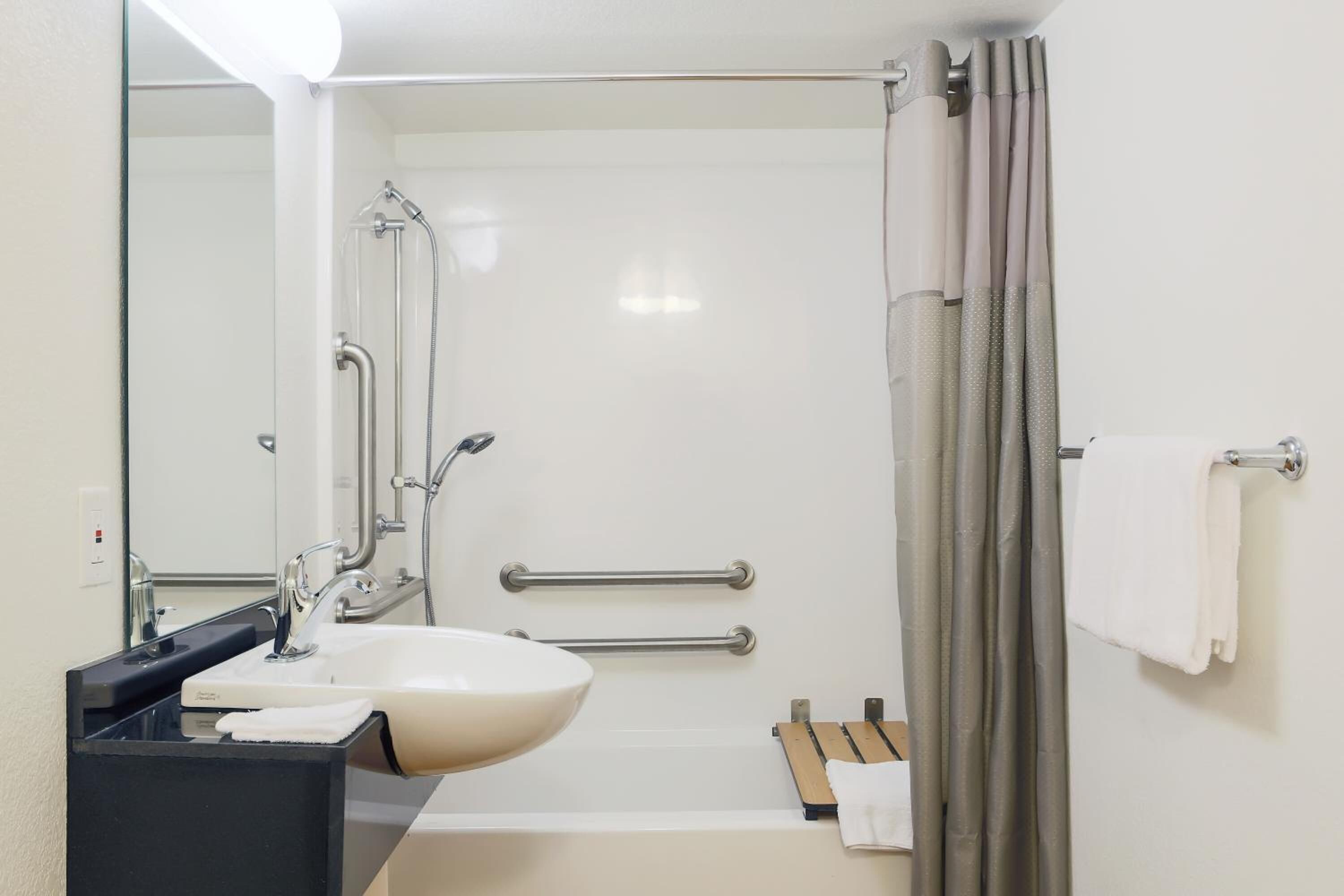 Un baño moderno con un lavabo blanco, un espejo, una ducha con puerta de cristal y un perchero para toallas.