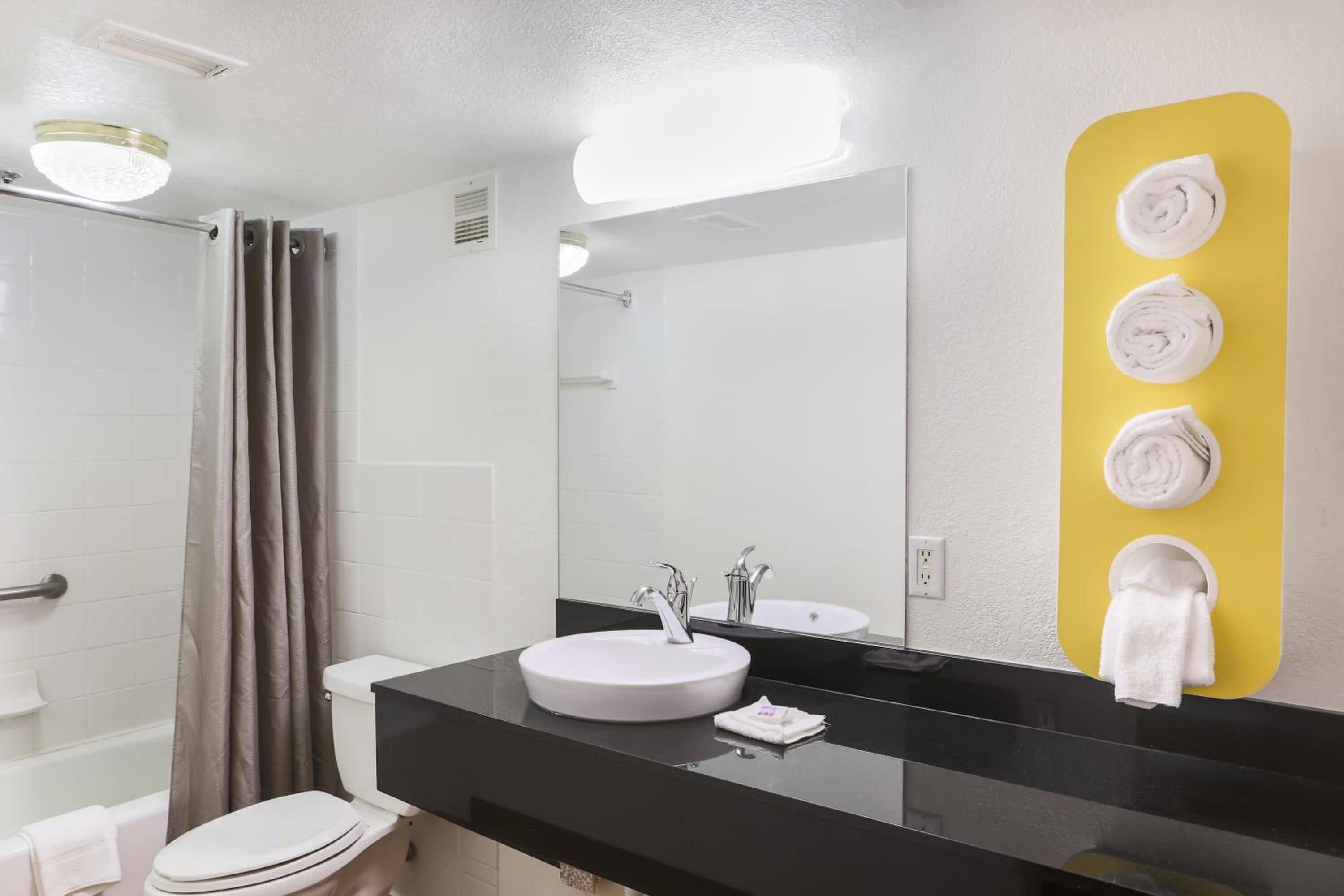A modern bathroom with a white sink, a large mirror, and a yellow towel rack.