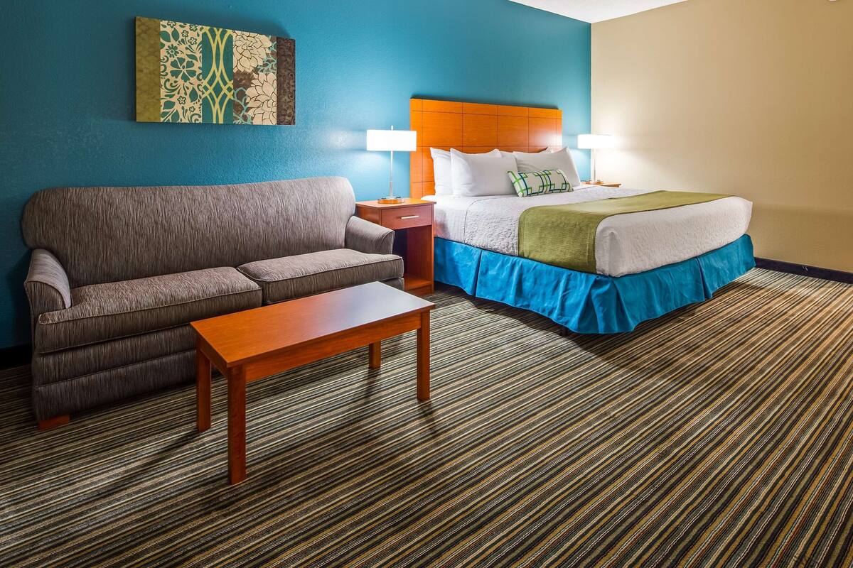 A hotel room with a sofa, a bed with a blue skirt, a wooden headboard, and a striped carpet.