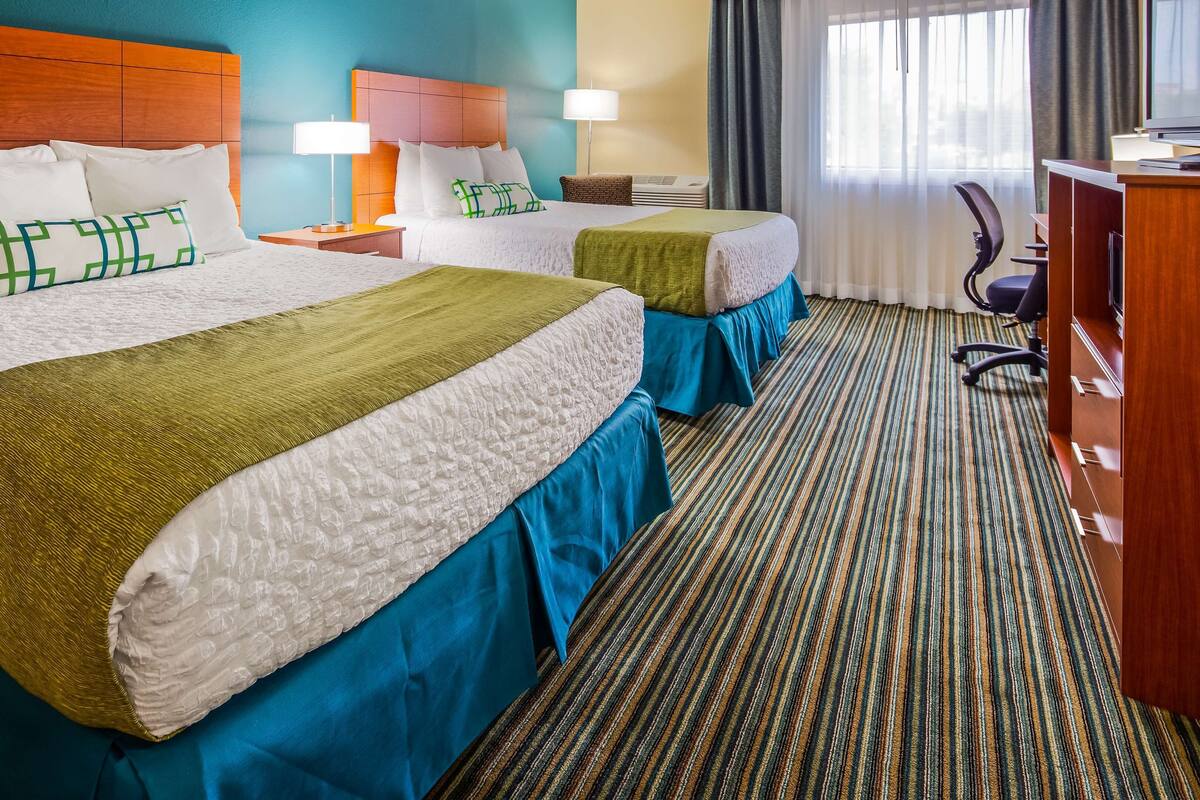 A hotel room with two beds, a desk, a chair, and a window with curtains.