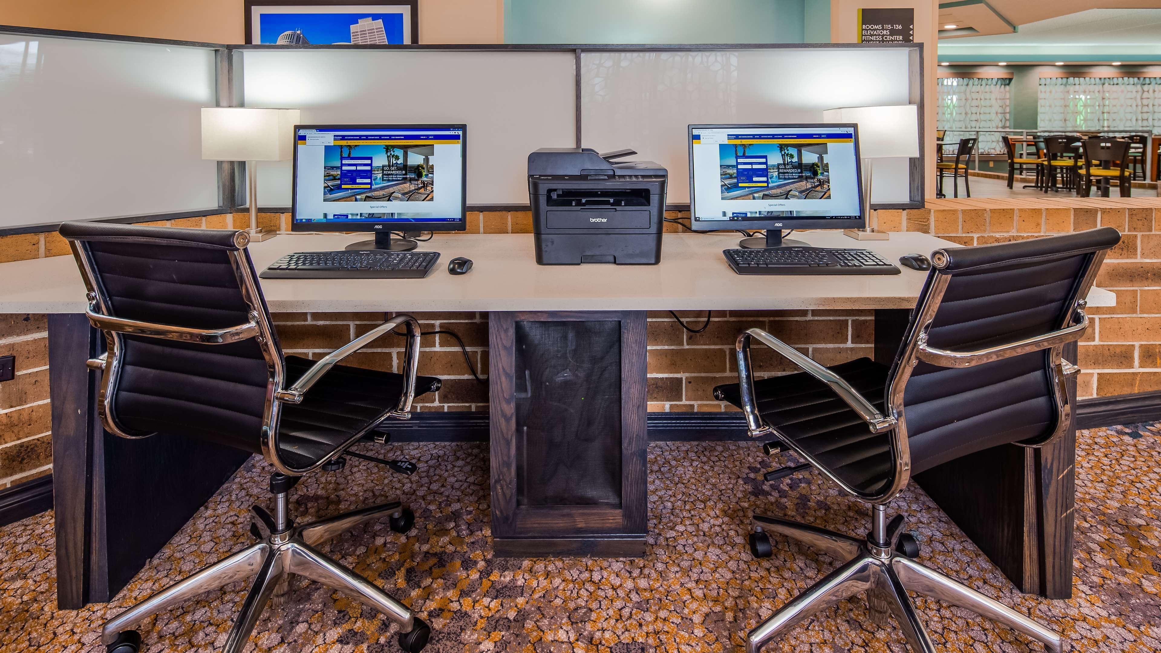 Un espacio de trabajo con dos computadoras, una impresora y dos sillas de oficina.