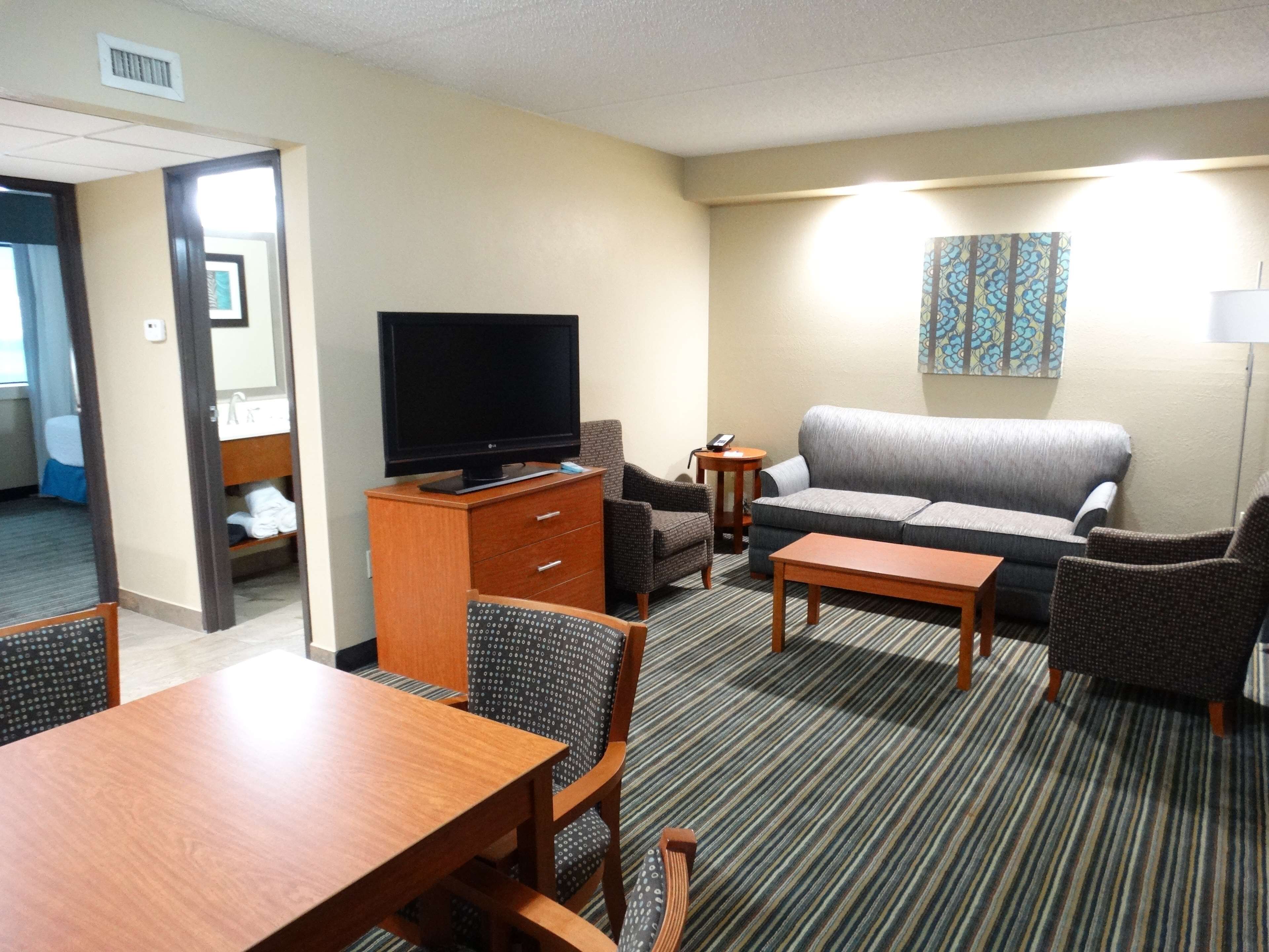 A hotel room with a TV, sofa, chairs, a table, and a painting on the wall.