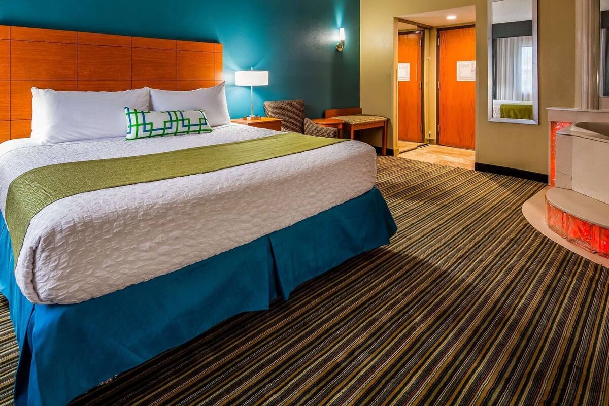 A hotel room with a large bed, a wooden headboard, a desk, a chair, and a small table.