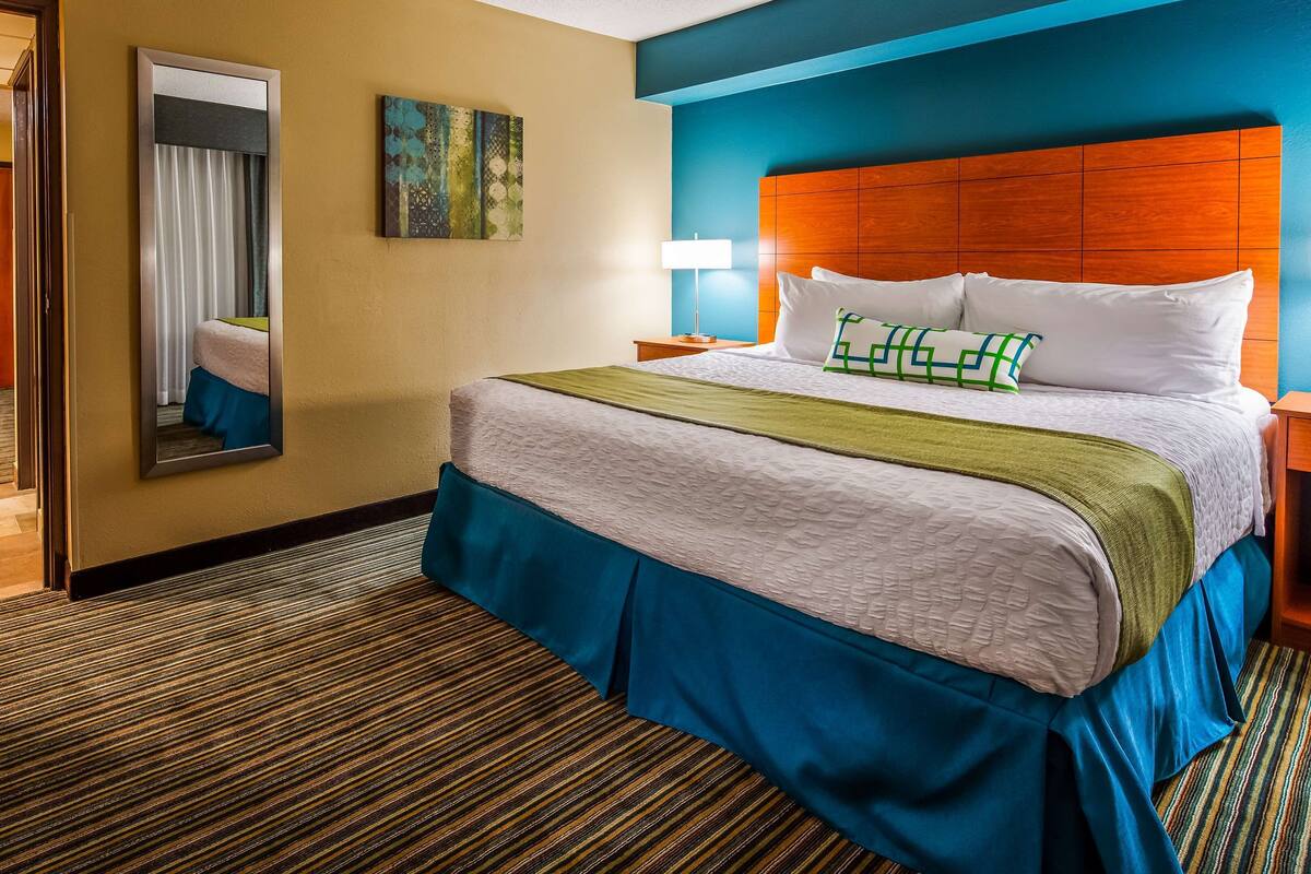 A hotel room with a large bed, a wooden headboard, a mirror, and a painting on the wall.