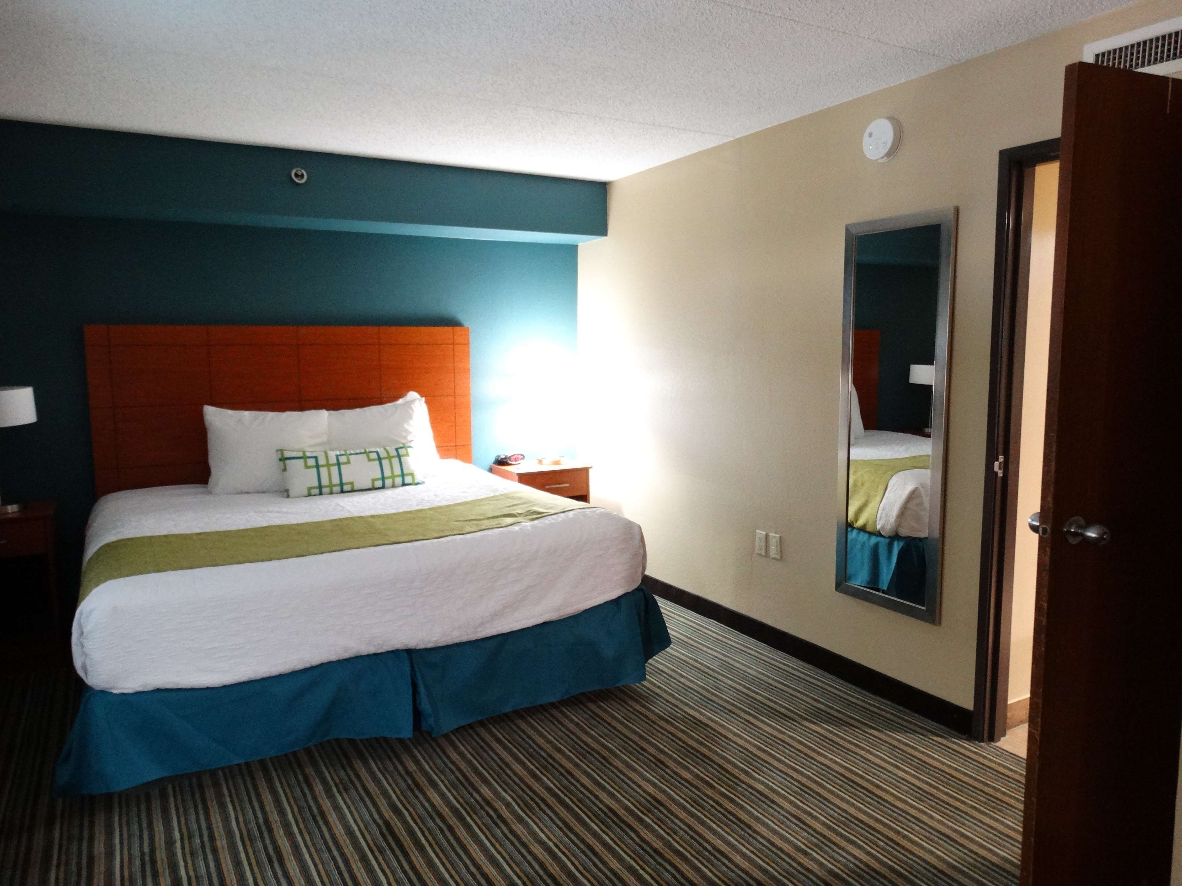 A hotel room with a large bed, a nightstand, a mirror, and a door.