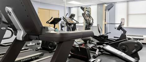 Une salle de sport équipée de tapis de course, de vélos elliptiques et de postes d'entraînement avec poids.