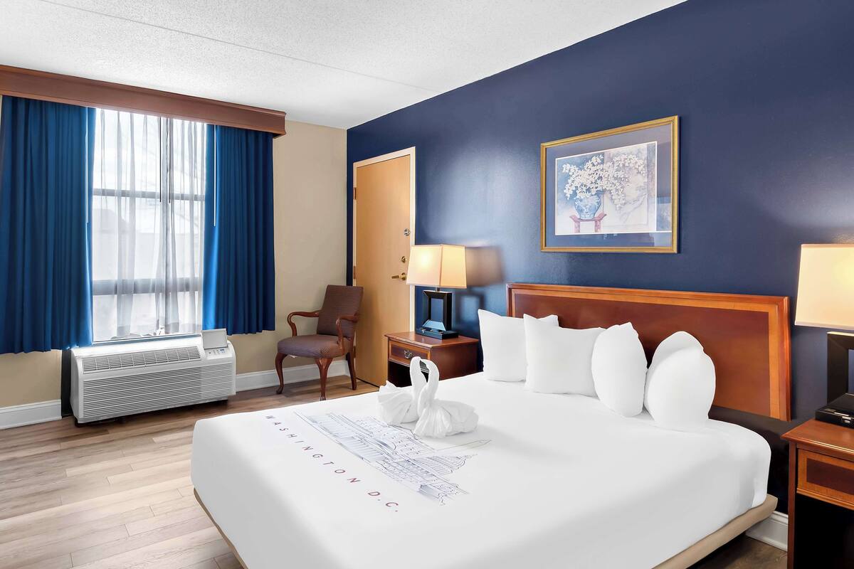 A hotel room with a large bed, a chair, a desk, a lamp, and a window with curtains.