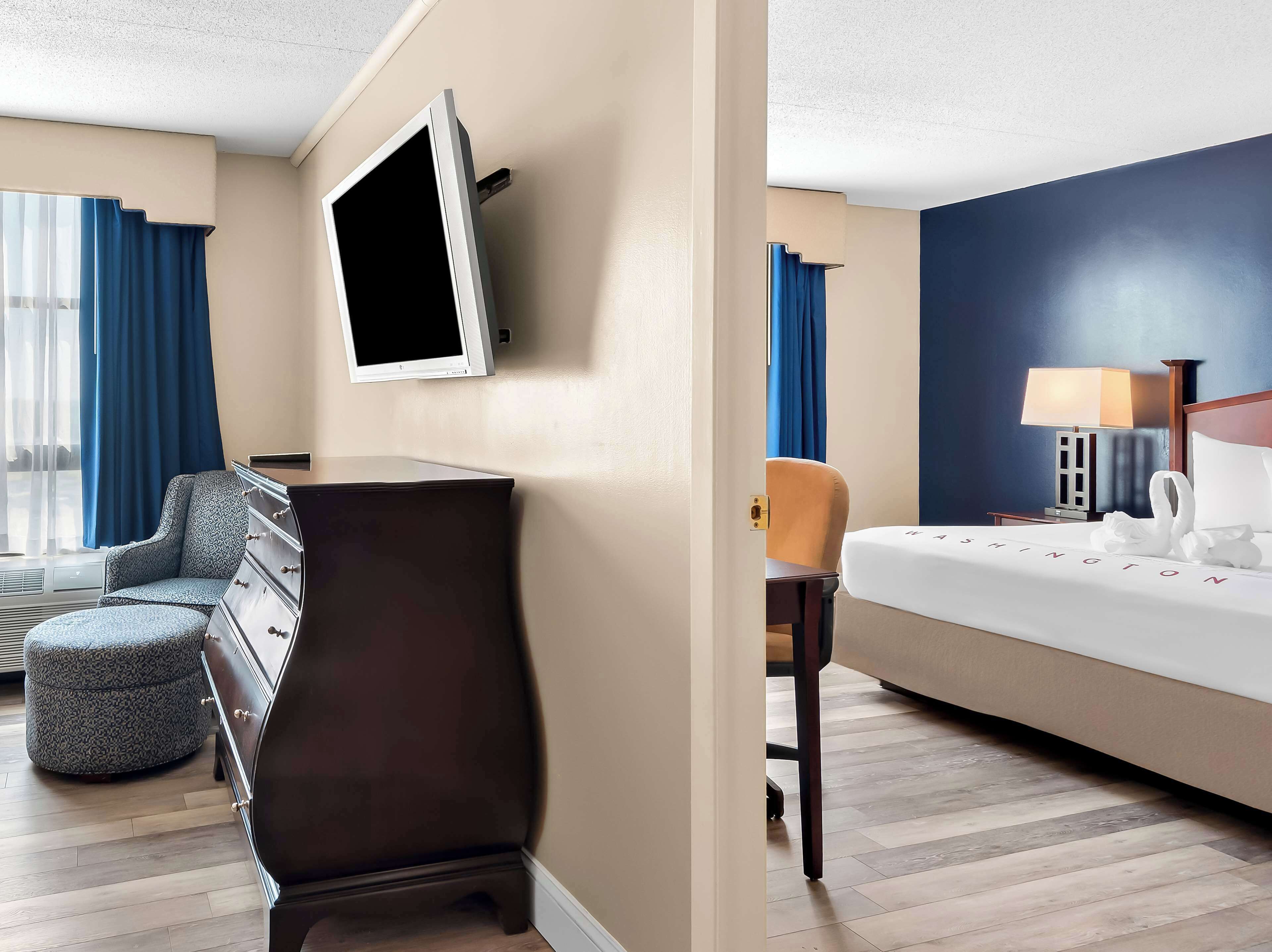 A hotel room with a bed, a desk, a chair, a TV, and a lamp.