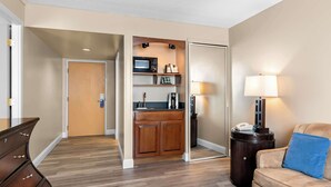 A hotel room with a wooden floor, a kitchenette with a microwave, a coffee maker, and a sink. There is a sofa with a blue pillow and a lamp. - Best Western Potomac Mills (Woodbridge)